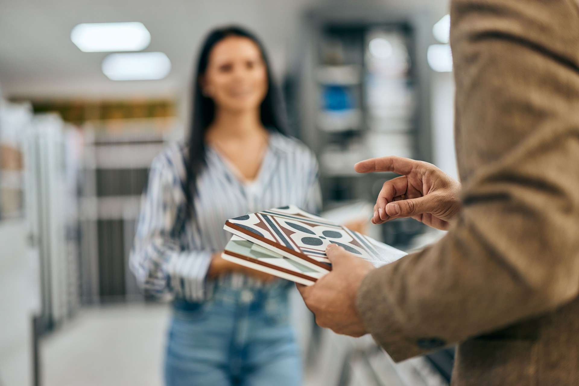 A woman in the background listening to the seller man, focuses on the ceramic tiles in his hands.